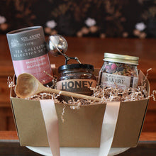 valentine's day basket with honey, a tea strainer, granola, a wooden heart spoon, and radiant glow tea