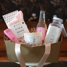 valentine's day basket with heart socks, a chocolate bar a candle, milk bath, and a sparkling drink 
