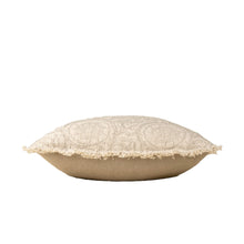 Beige textured pillow with intricate floral pattern and fringe trim on its side on a white background