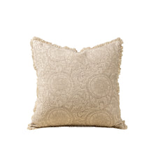 Beige textured pillow with intricate floral pattern and fringe trim on a white background