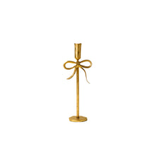 tall gold candle holder with bow design on a white background