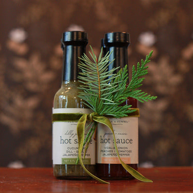 four pack of hot sauces bundled together in a green velvet ribbon with winter greenery