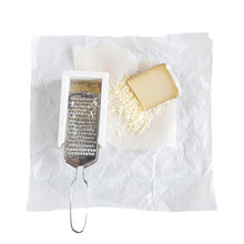stainless steel cheese grater and white marble container with grated cheese on white wax paper