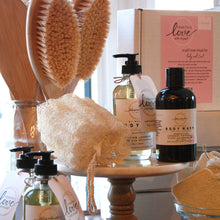 Bath products including bottles, a loofah, and brushes on a stand with a pink box in the background.