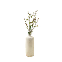 Artificial plant branch with green leaves and small berries placed in a small vase on a white background