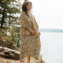 Woman in a yellow floral dress standing by a body of water with trees in the background
