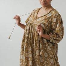 Woman wearing a floral dress holding its tassel strings against a plain background